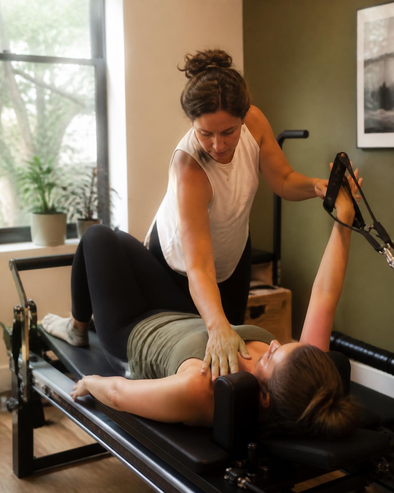 An instructor adjusting a client's shoulder position on the reformer